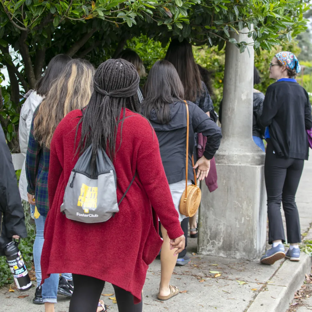 multiple young people with different identities walking on sidewalk lined with trees 