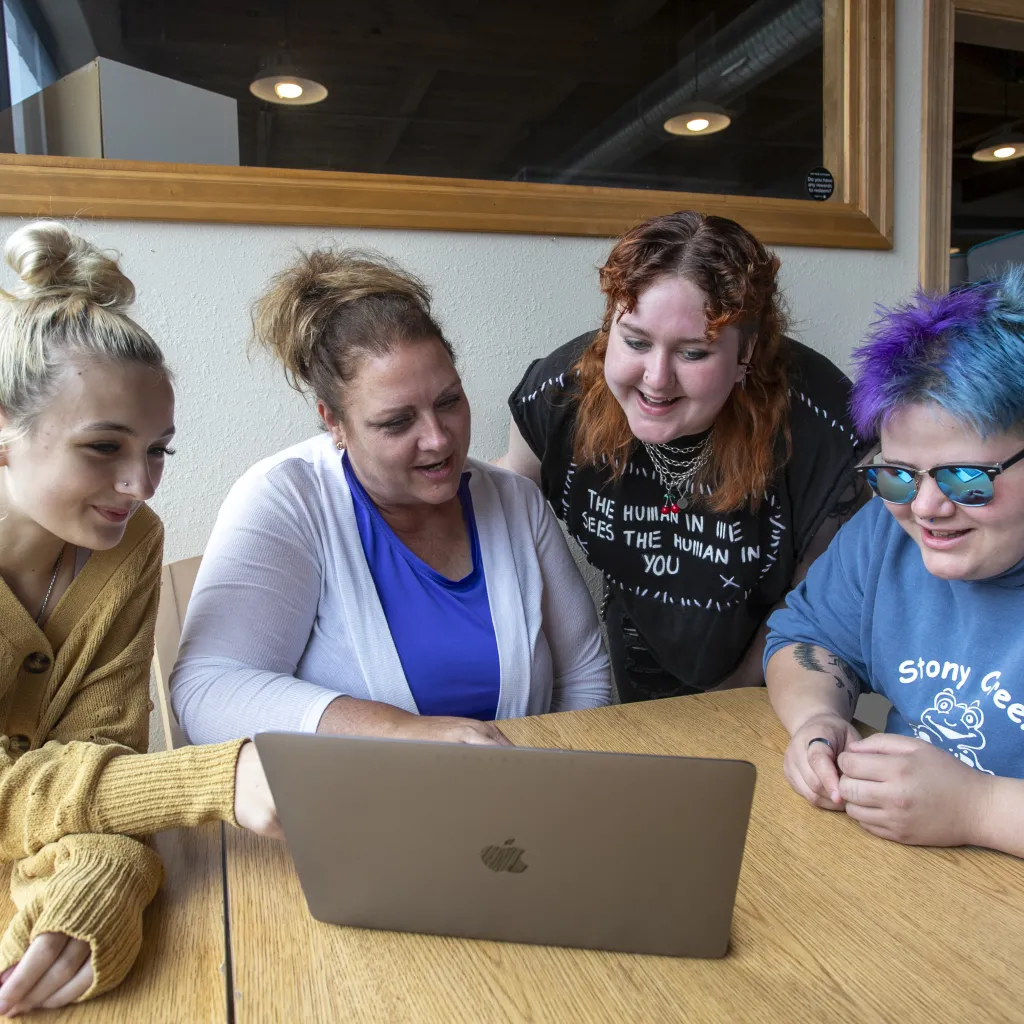 young people sitting around a laptop computer with an adult smiling