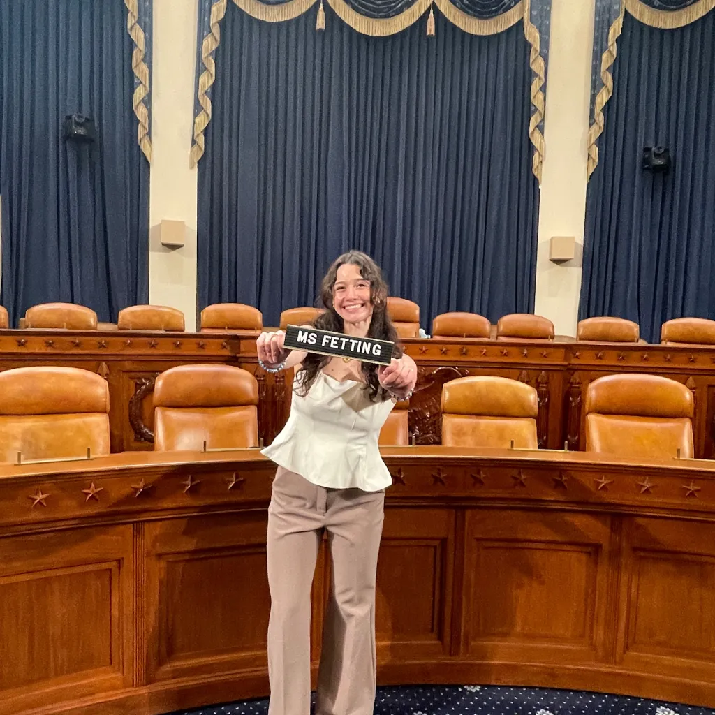 Young adult holding placard with Ms. Fetting on it in Congressional Hearing Room 