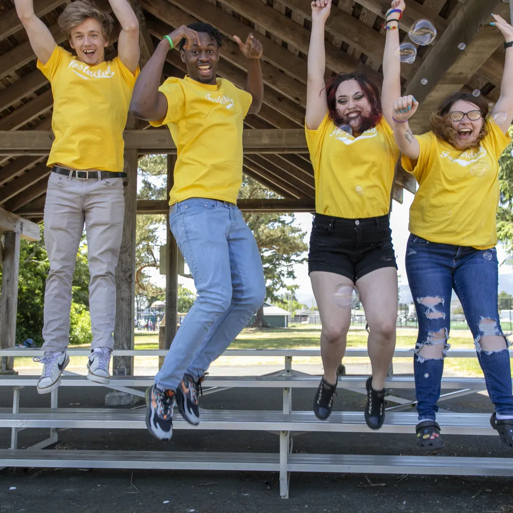4 youth in yellow shirts jumping with arms raised. 