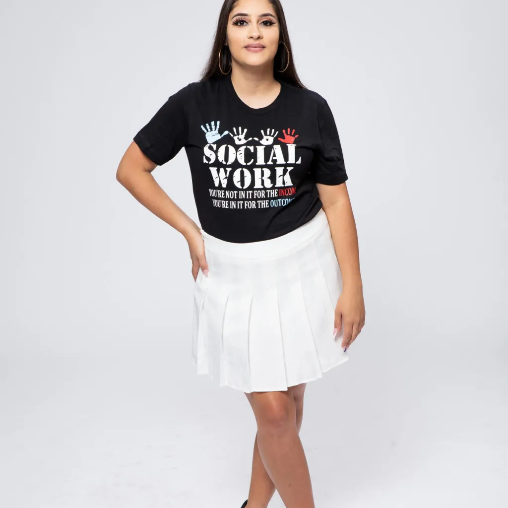 Mayda Berrios stands against white background with black t-shirt that says "Social Work - You're not in it for the income. You're in it for the outcome." 4 handprints are on the t-shirt as well.